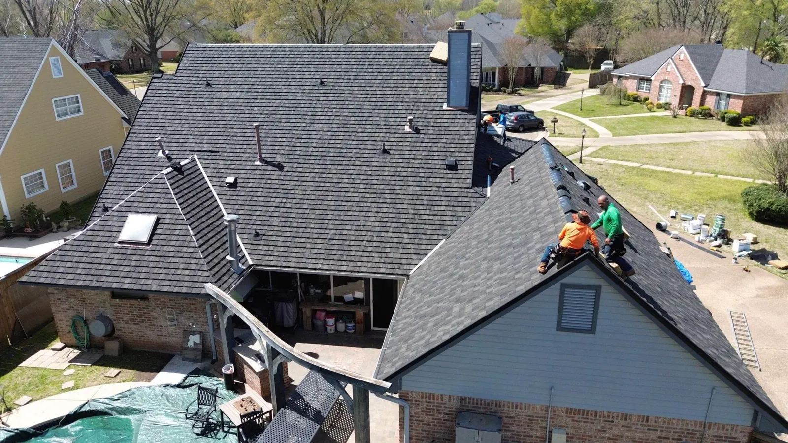 Drone view of a crew laying new dark shingles on a house roof