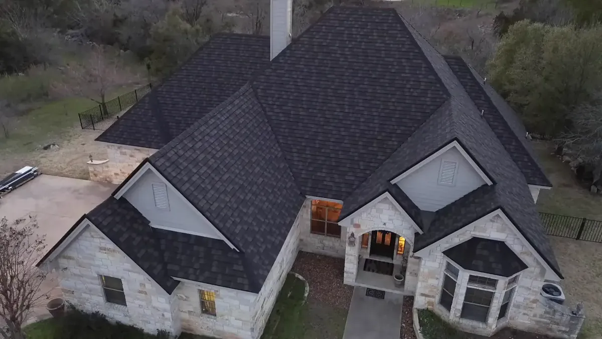 Finished dark architectural shingle roof on a stone house, seen from above at dusk
