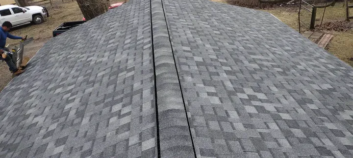 Looking down the ridge of a gray architectural shingle roof, with a worker and a white pickup truck below