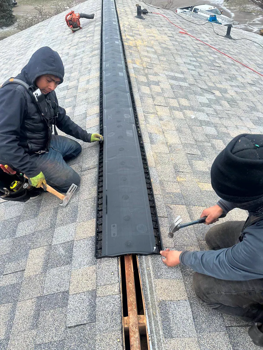 Two roofers fastening a ridge vent along the peak of a roof
