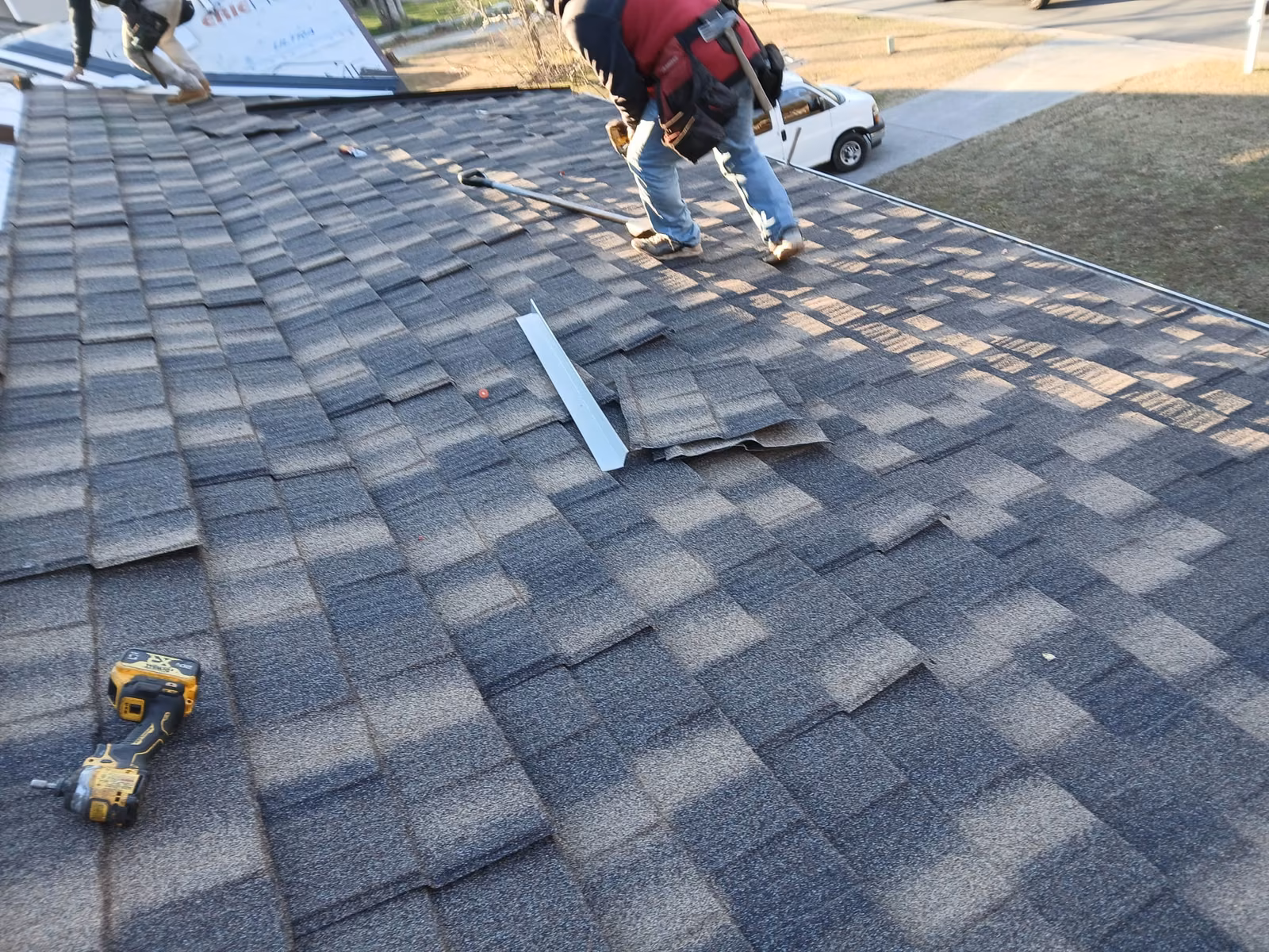 Roofers working across a gray shingle roof, a nail gun resting on the shingles