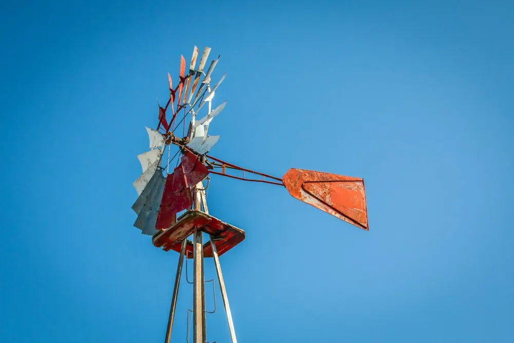 The red and white vanes and tail of a water-pump windmill against a clear blue sky