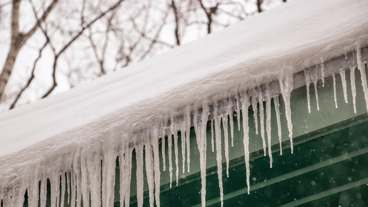 Icicles hanging from the eave of a roof under a thick layer of snow