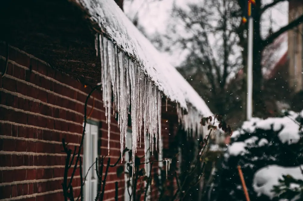 Long icicles hanging from a snow-covered roof edge over a brick wall