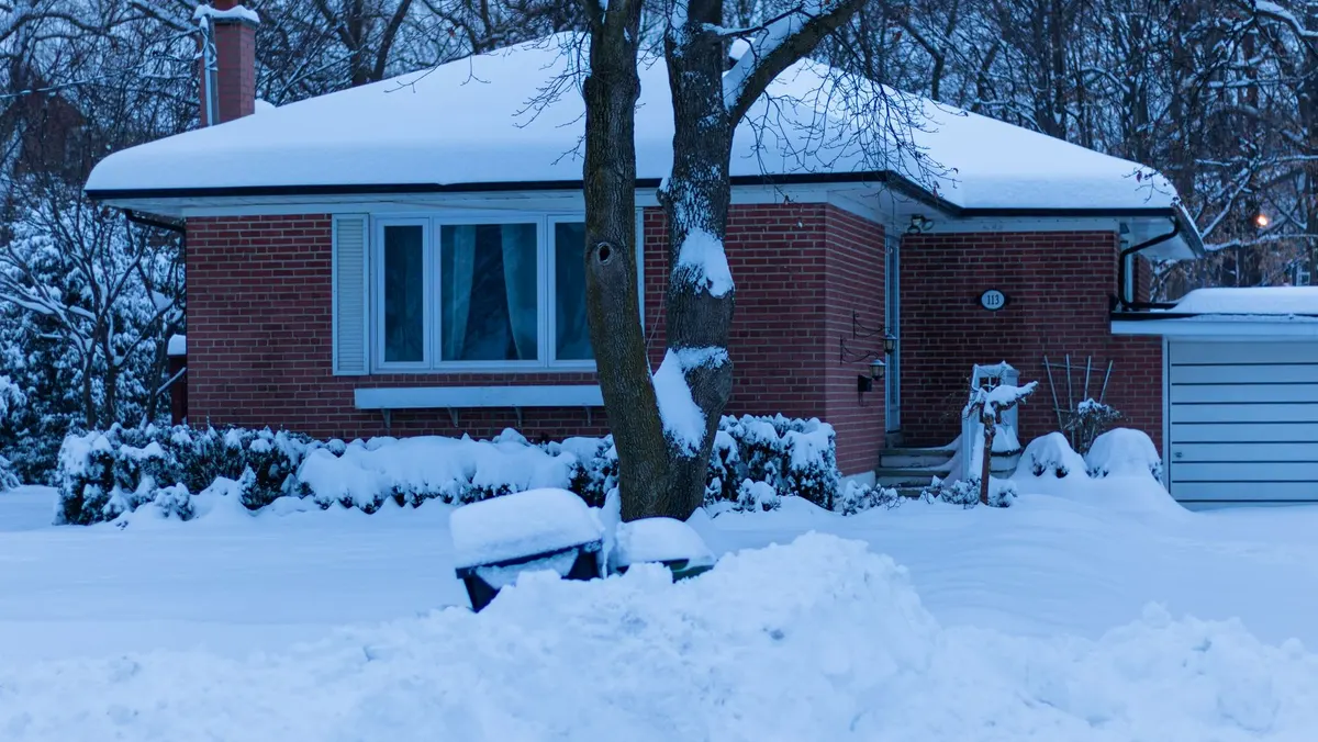 Brick ranch house with a deep layer of snow on its roof at dusk