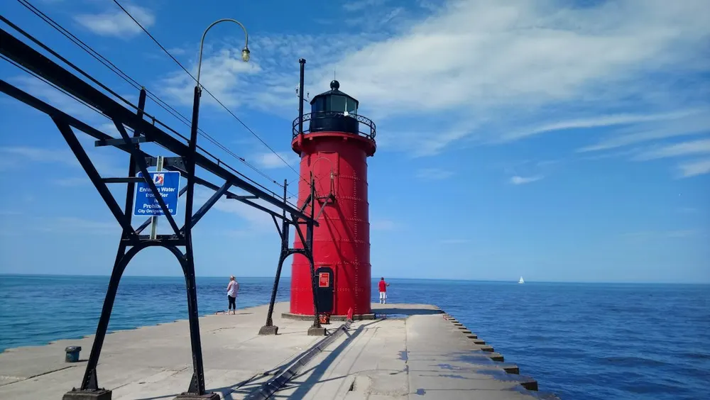 The red pier lighthouse at South Haven and its black steel catwalk, Lake Michigan on both sides under a blue sky