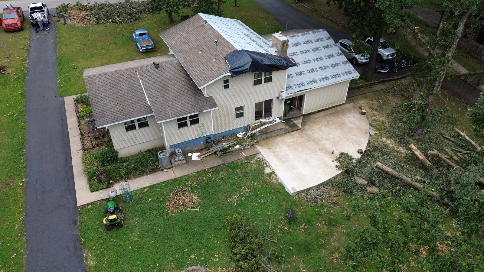 Aerial view of a storm-damaged roof covered in tarps and wrap