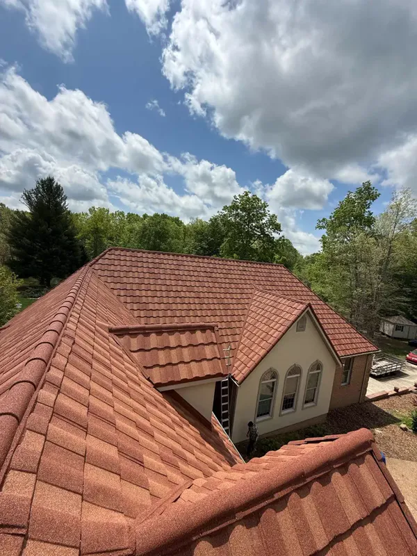 Terracotta-colored stone-coated steel tile roof on a cream house among green trees