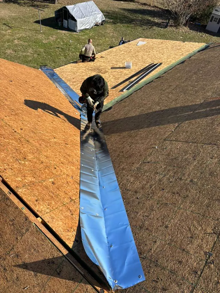 Roofer laying metal flashing down a roof valley over fresh decking